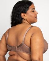 Woman wearing a beige bralette against a plain background